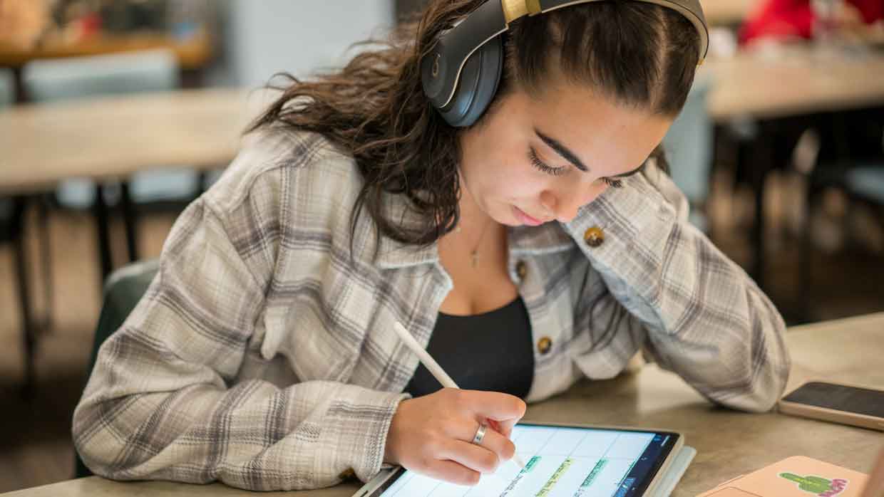 Female student working on a tablet with headphones on. 
