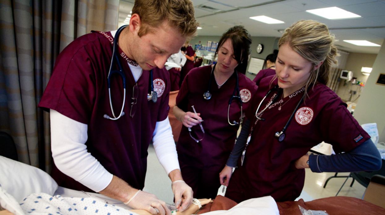 Three nurse practitioners at MCPHS working with a manikin