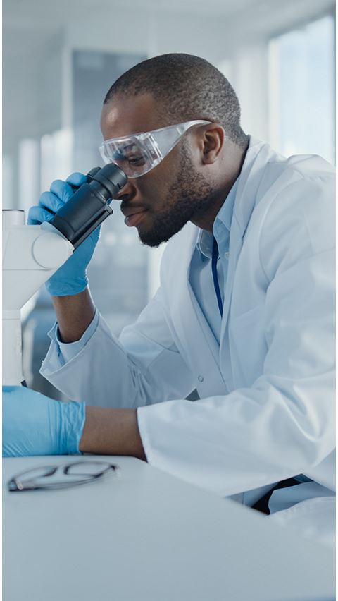 Male in lab looking into a microscope. 