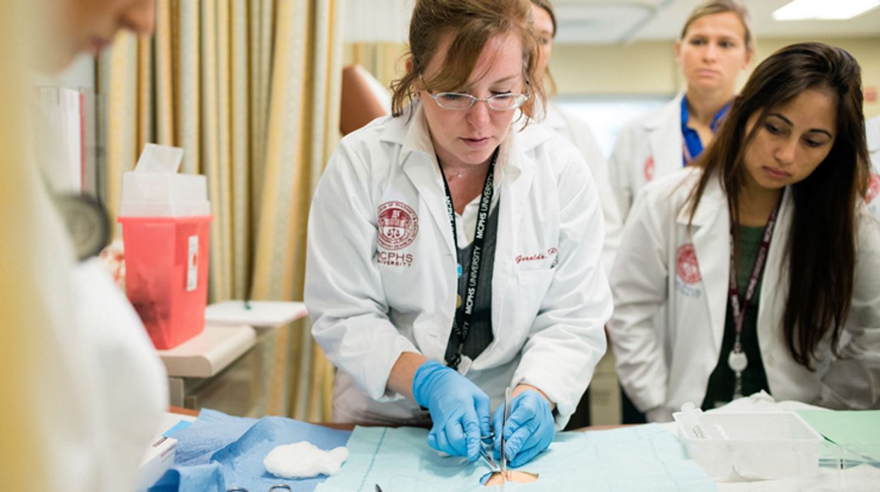A group of MCPHS physician assistant students observe a professor performing a procedure demonstration