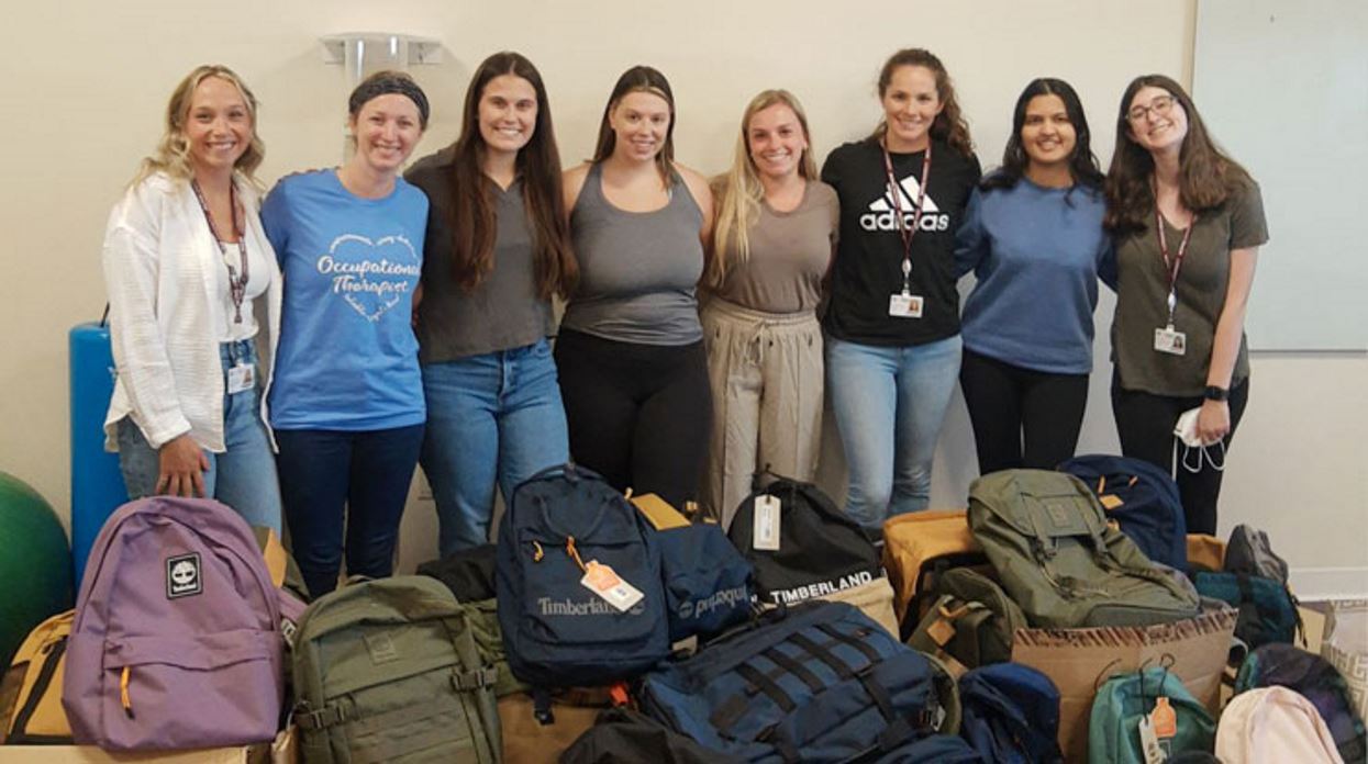 Members of the Coalition of Occupational Therapy Advocates for Diversity (COTAD) at MCPHS pose in front of backpacks full of school supplies