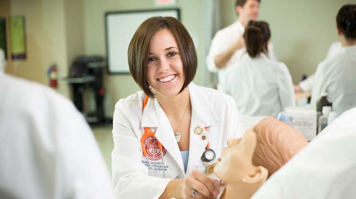 Smiling physician assistant student in an MCPHS classroom working with a patient simulator manikin