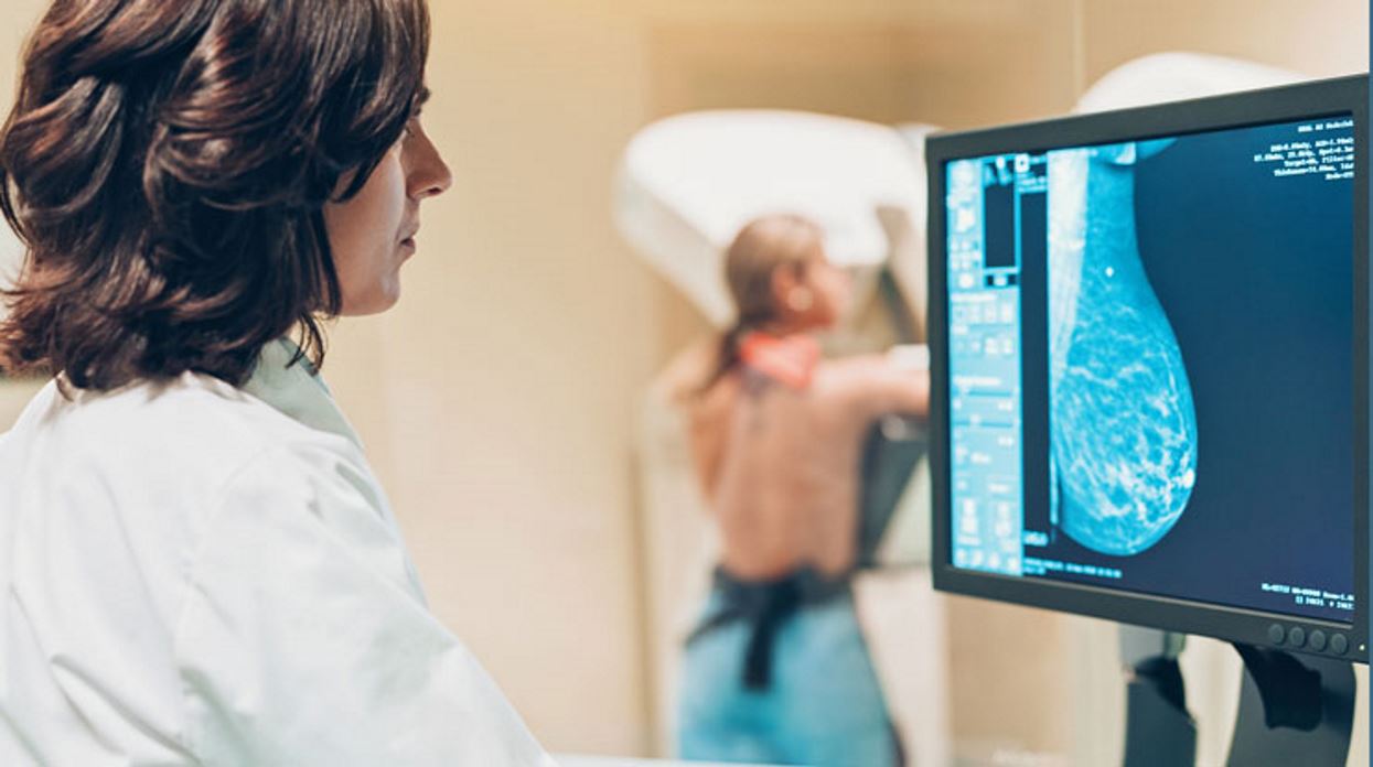 Woman has a mammogram while another woman reviews the breast scan on a screen