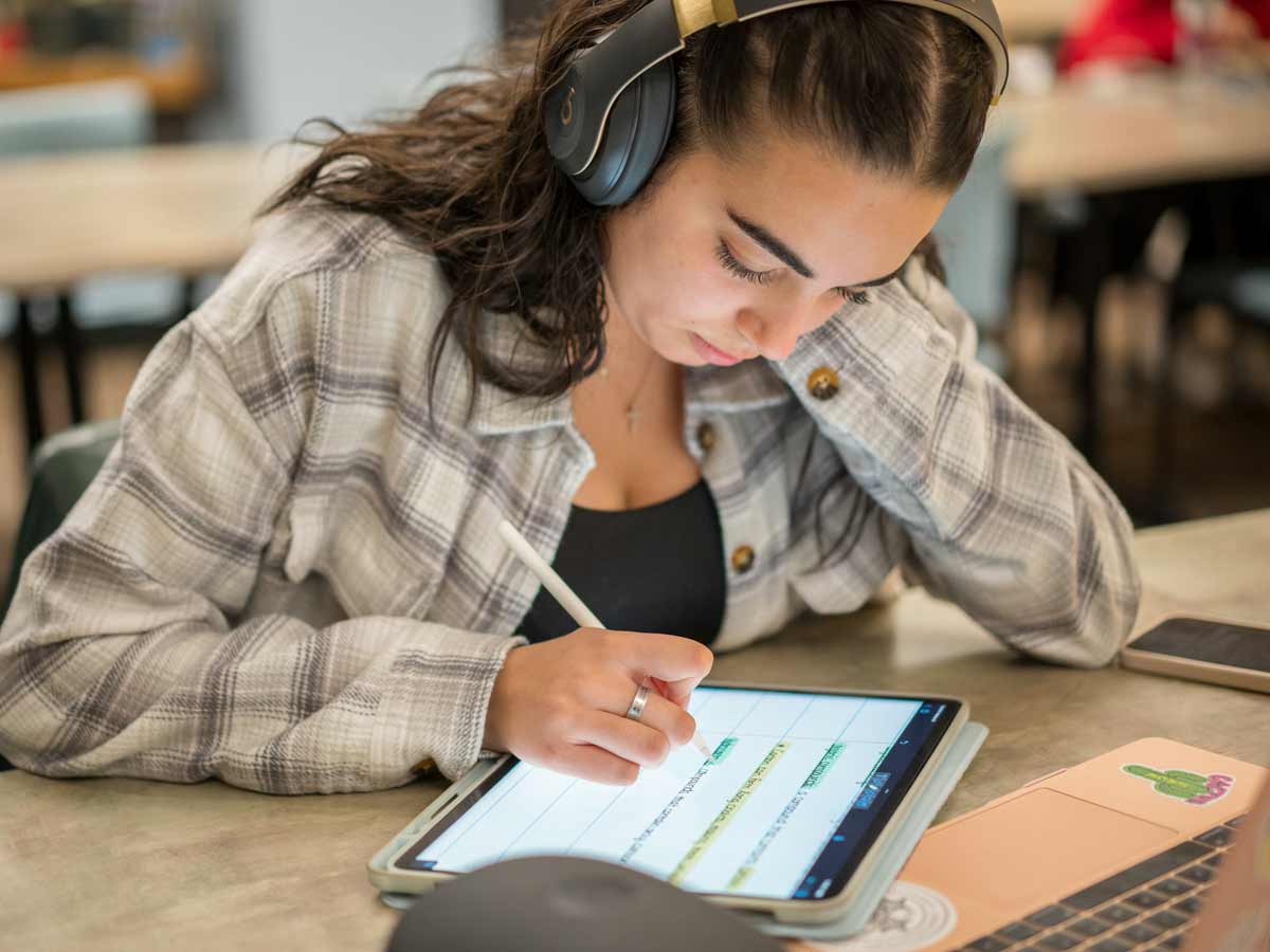 Female student working on a tablet with headphones on. 